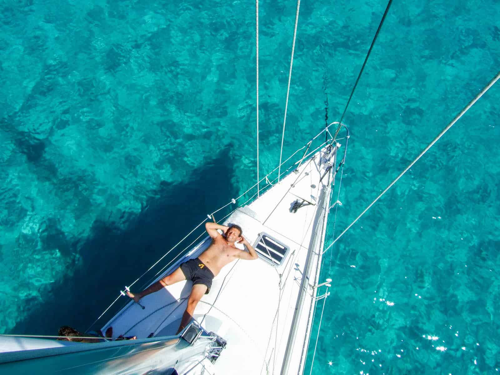 Sereno momento di relax a prua di una barca a vela durante una crociera estiva in Sardegna.
